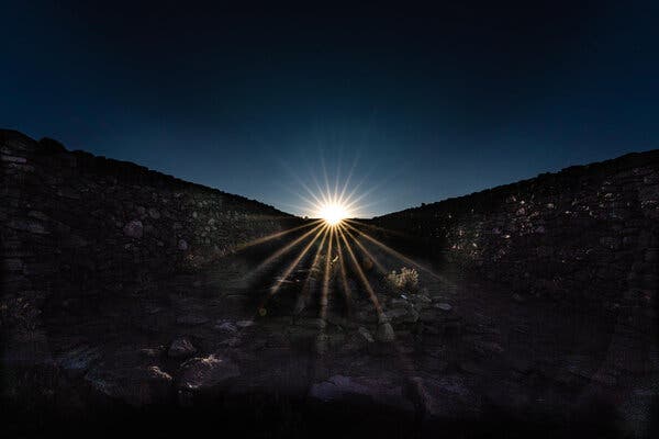 A glinting sun rising over a darkened hillside.